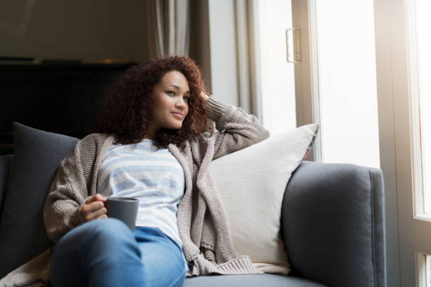 istock Thoughtful young woman sitting with coffee on sofa 1058670474