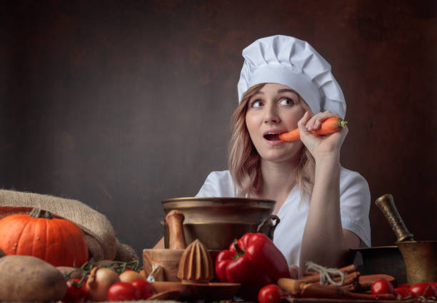 istock Young beautiful girl in a chef's uniform eating carrots. 1058684520