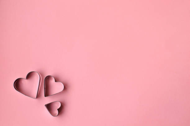 Three heart shaped cookie cutters over a pink background. Valentine's Day.