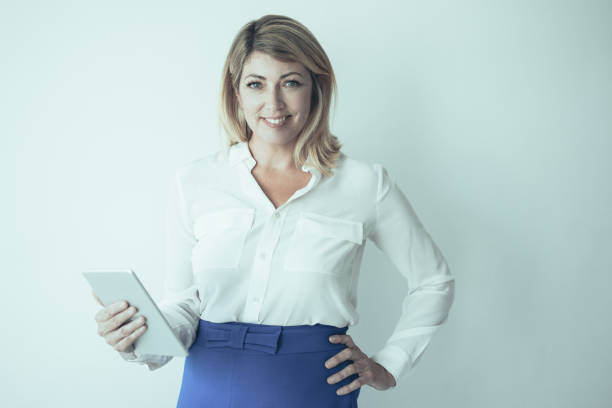 Closeup portrait of smiling middle-aged attractive fair-haired woman looking at camera and holding tablet computer. Technology concept. Isolated front view on grey background.