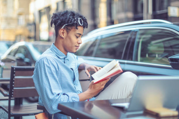 istock Young student is flipping up a book in a sidewalk caffee 1058709348