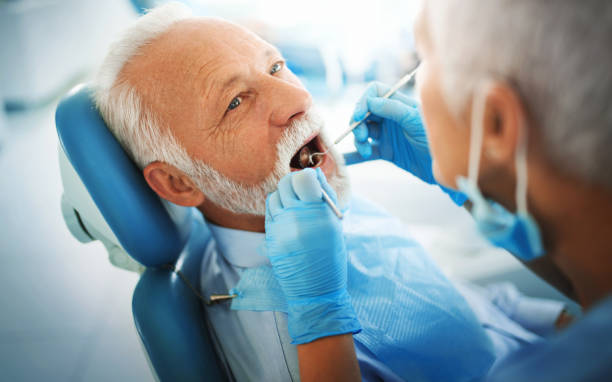 Dentist appointment. Closeup side view of a mid 50's female dentist examining an early 60's male patient. The dentist is using angled mirror and dental probe and checking the inner side of patient's lower jaw teeth. dentists chair stock pictures, royalty-free photos & images