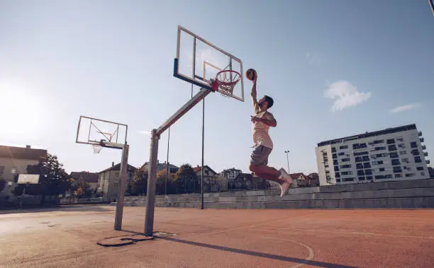 Young man jumping and making a fantastic slam dunk playing street ball, basketball. Urban authentic.