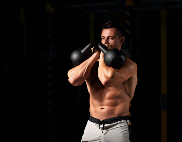istock Handsome strong man doing the exercises with kettlebells on dark shadow background. Closeup contrast portrait. 1058719802