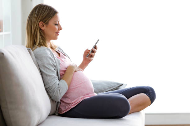 mensagens de mulher grávida bonita com seu smartphone no sofá em casa - new mother - fotografias e filmes do acervo