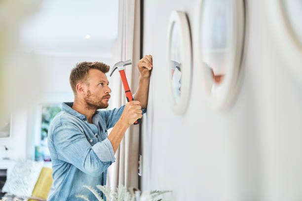 Handsome young man hammering nail on white wall