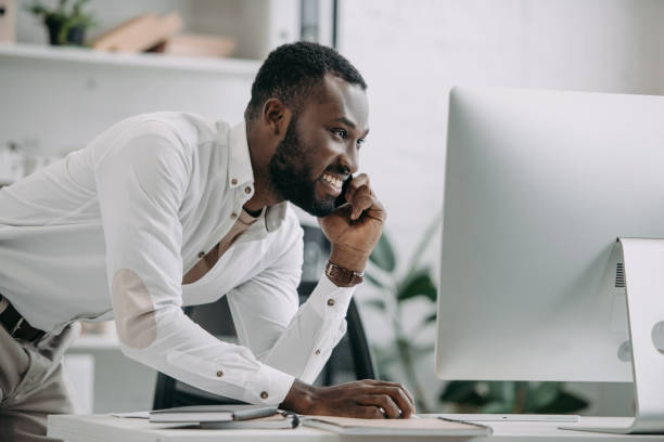 istock side view of handsome african american businessman talking by smartphone and using computer in office 1058759784