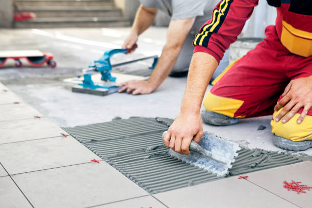 ceramic tiles. tiler placing ceramic wall tile in position over adhesive, with handy man in background cutting ceramic tile. - tile adhesive imagens e fotografias de stock