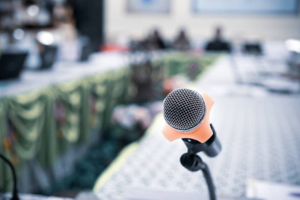 istock Microphones on abstract blurred of speech in seminar room or front speaking conference hall light, blur chairs for people in event meeting convention hall in hotel background 1058764954