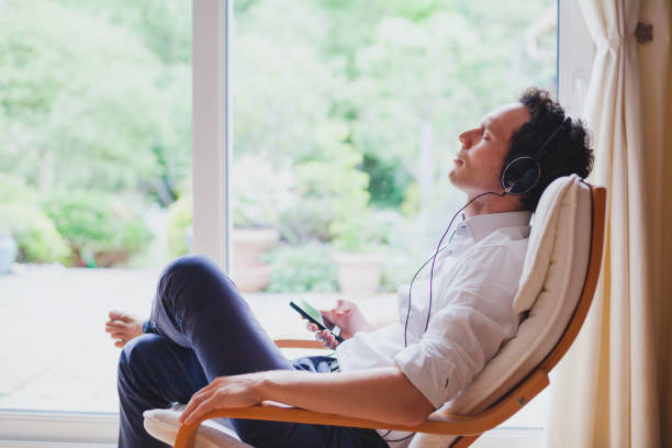 Listen relaxing music at home, relaxed man sitting in headphones. listening relaxing music at home, relaxed man in headphones sitting in deck chair in modern bright interior german ethnicity stock pictures, royalty-free photos & images