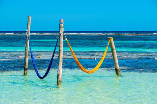 Two colourful and unused hammocks suspended from wooden posts in Caribbean Sea