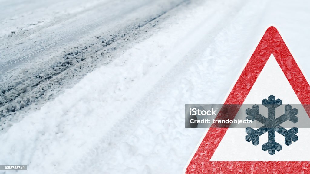 Winter Driving - Caution - Risk of Snow and Ice Winter Driving - snowy road with tire tracks and warning sign Winter Stock Photo