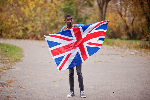 African man in africa traditional shirt on autumn park with Great Britain flag.