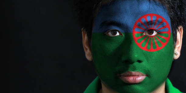 Portrait of a man with the flag of the Romani people painted on his face on black background. stock photo