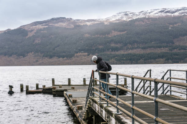 istock Man is looking down off the pier on Loch Lomond 1058793428
