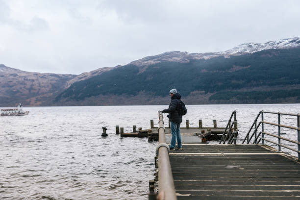 istock Man is looking to the side from the pier on Loch Lomond 1058793432