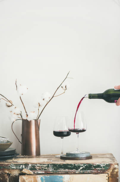 Red wine pouring from bottle in man's hand, copy space Red wine pouring from bottle in man's hand into wineglass over rustic kitchen countertop, white background behind, copy space, vertical composition. Wine shop, winery, bojole nouveau holiday concept wine bar counter stock pictures, royalty-free photos & images