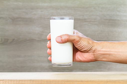 Hand holding glass of fresh milk on blurred wooden background