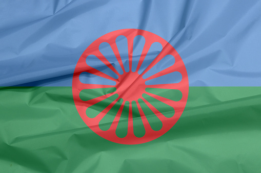 Fabric flag of Romani people. Crease of the Gypsies flag background, blue and green background, representing the heavens and earth and red chakra or cartwheel in the center.