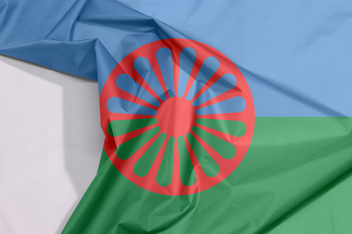 Romani people fabric flag crepe and crease with white space, blue and green background, representing the heavens and earth and red chakra or cartwheel in the center.