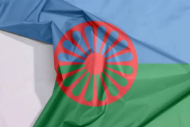 Romani people fabric flag crepe and crease with white space, blue and green background, representing the heavens and earth and red chakra or cartwheel in the center.