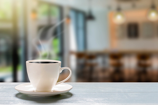Hot cup of coffee on wooden desk on blurred coffee shop background