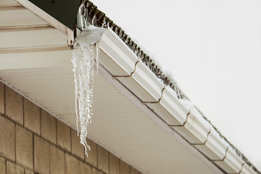 Roof cornice with overhang icy icicle gutter after thaw