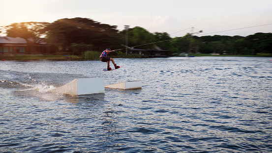 Bueng Taco, Bangkok, Thailand. October 19th 2018. Asian male jumping on the ramp with his wake board in a blurred motion background in the afternoon sunset.