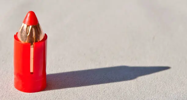 A 50 caliber sabot bullet for a muzzle loader rifle in a plastic red casing casting a shadow on a white background