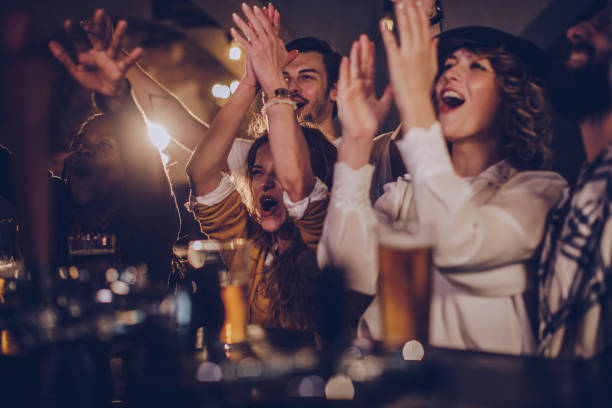 Friends in pub watching match Group of friends cheering with beer in a pub bar counter photos stock pictures, royalty-free photos & images