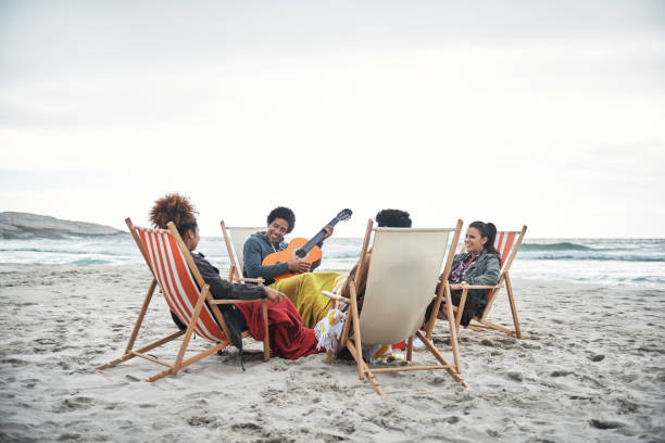 Shot of a young man playing the guitar while hanging out with friends at the beach