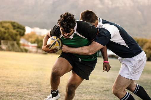 Professional rugby players striving to get the ball during the game. Rugby player with ball is blocked by the opposite team player at ground.