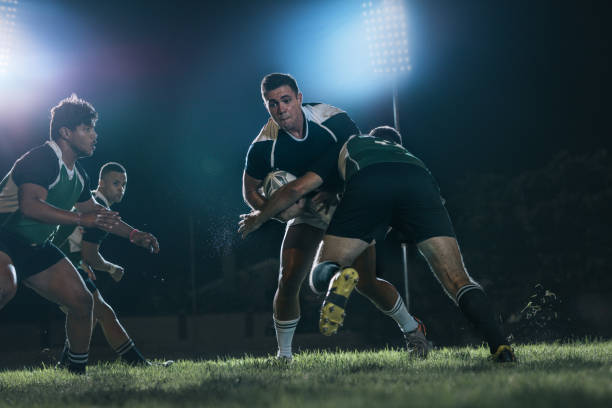 Intense rugby action at sports arena Strong rugby players fighting for the ball during the game. Intense rugby action under lights at sports arena. rugby stock pictures, royalty-free photos & images