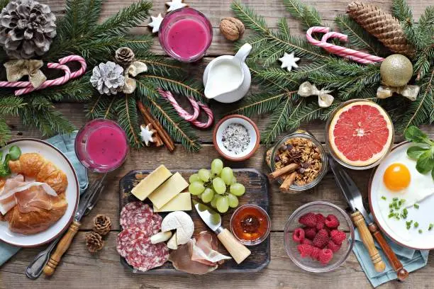 Christmas brunch or breakfast table. Festive brunch set, meal variety with fried egg, appetizers platter, croissant, granola, smoothy and traditional sweets . Overhead view