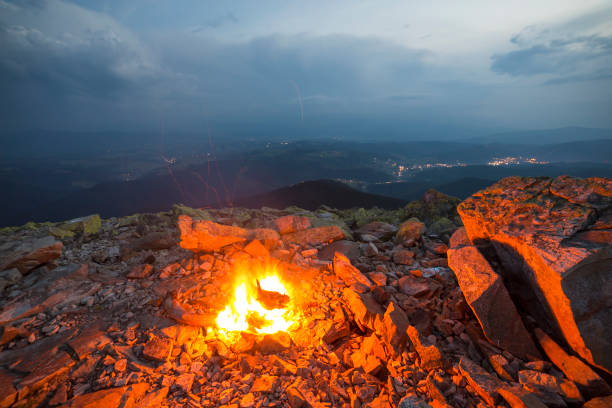 istock Beautiful summer night in mountain. Bright fire burns on rocky mountain top under blue cloudy sky. 1058838108