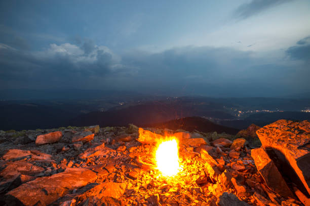 istock Beautiful summer night in mountain. Bright fire burns on rocky mountain top under blue cloudy sky. 1058838126