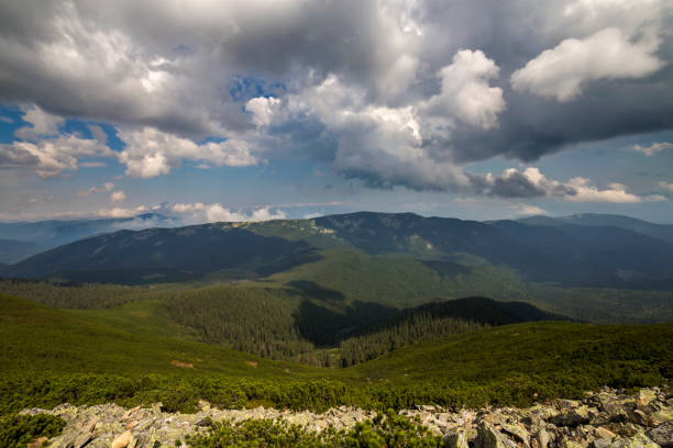 istock Bright white puffy clouds lit by sun spreading against blue summer sky over green mountain ridge. 1058838160