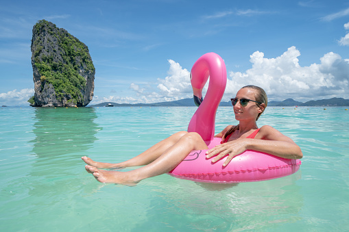 Young woman relaxing on idyllic beach with inflatable flamingo playing in pristine clear water in the Islands of Thailand. People travel luxury fun and cool attitude concept