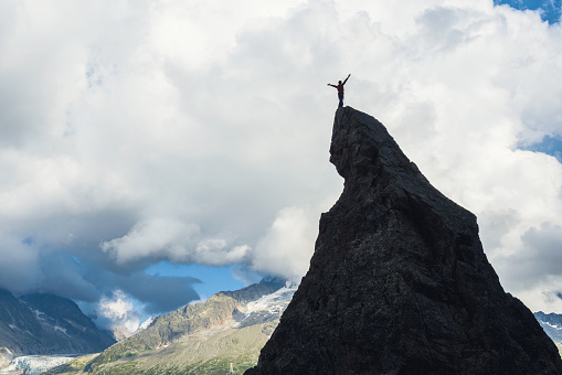 Climber standing with arms upstretched on top of a mountain pinnacle