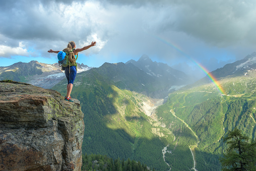 Woman celebrating her success in climbing the mountain in front of a colorful rainbow