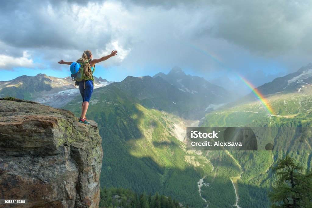 woman celebrating success on the mountain Woman celebrating her success in climbing the mountain in front of a colorful rainbow Rainbow Stock Photo
