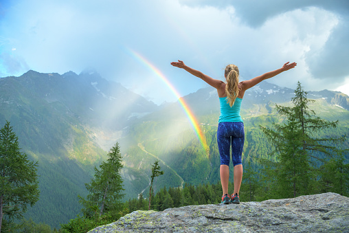 Young woman enjoying a colorful rainbow in the mountains during a summer rain