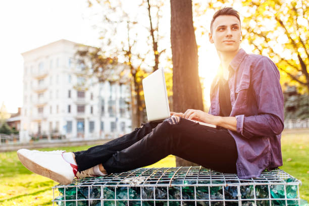 istock a man in casual clothes sits on a bench, works with a laptop and communicates with wireless headphones, 1058846546