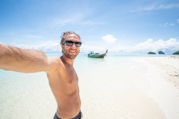 istock Cool young man takes selfie on tropical beach having fun on vacations 1058856118