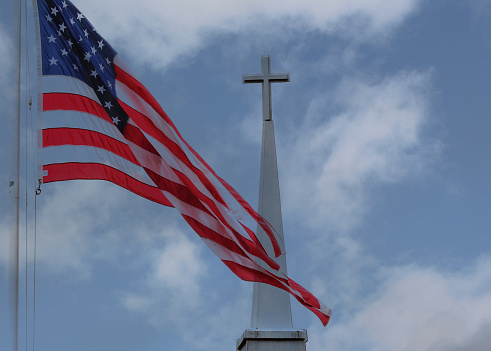 The American Flag flies over a steeple with the Christian Cross