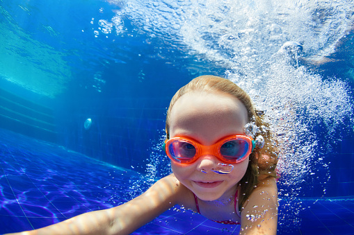 Happy family in swimming pool. Smiling child in goggles swim, dive in pool with fun - jump deep down underwater. Healthy lifestyle, people water sport activity, swimming lessons on holidays with kids