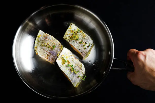 A hand holding three fish fillets with herbs and spices in a pan ready to be fried.