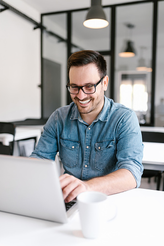 Smiling young man using laptop in modern office.