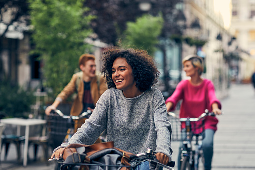Friends Riding Bicycles In A City. Cycling in pedestrian zone and smiling. Focus on African Woman on Front