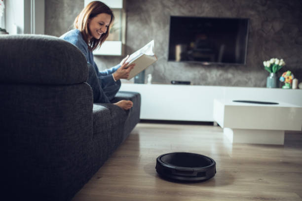 istock Woman reading book while robotic vacuum cleaner cleaning room 1058888518
